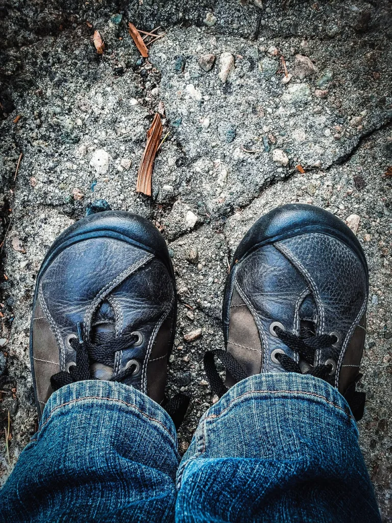 Widok z góry na ciemne buty i nogawki dżinsów na kamienistej ścieżce.